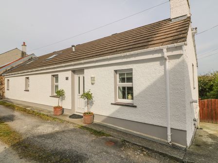 A white single-story house with a sloped roof two potted plants near the entrance at Tyn Y Giat in Brynsiencyn near Beaumaris