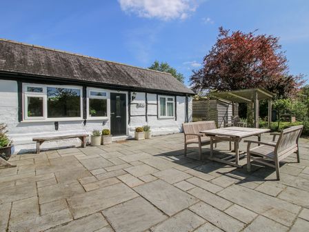 An outdoor patio area with wooden table and chairs outside a white house with black door at The Old Beams at Pont y Forwyn in Llansantffraidd-ym-Mechain near Welshpool