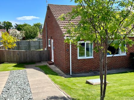 A brick house with a tiled roof a front yard with grass a tree a pathway with stones and wooden fences at Araucaria House in Whitby