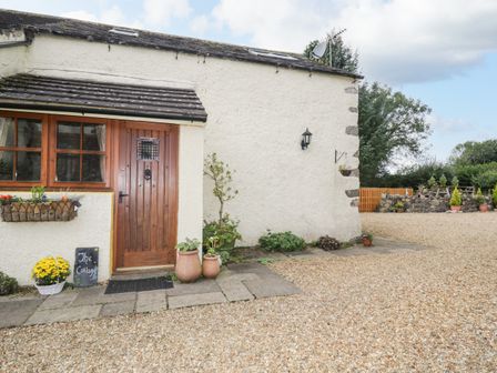 The exterior of a cottage with a wooden door stone pathway and potted plants at The Cottage at Graysondale Farm Cockermouth