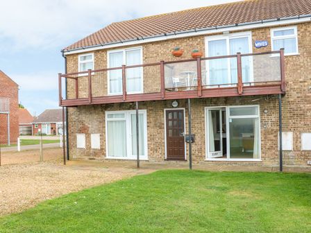 A two story brick building with balconies and patio doors on a grassy lawn at Surf in Hunstanton