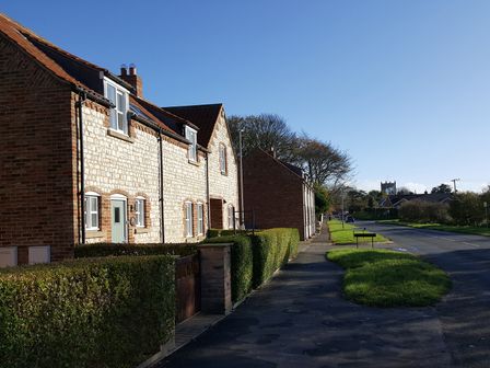A street view with stone houses hedges sidewalk and a distant church tower at Pebble Cottage Dunnscroft in Flamborough