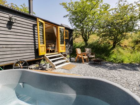 An outdoor area with a wooden hut with open doors two wooden chairs a fire pit and a small pool at Moelfre - Shepherds Hut in Llanbedr
