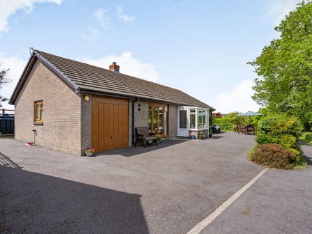 A single story brick house with a garage and a paved driveway with outdoor seating and greenery at Yr Hen Ffald Pontarddulais