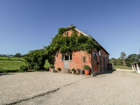 A brick building with plants growing over the entrance and potted plants outside on a gravel driveway at Breaches Barn in Rockbourne near Fordingbridge
