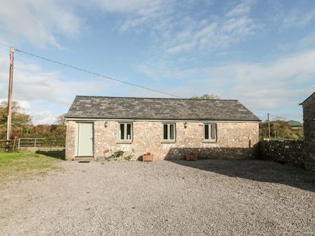 Exterior view of a stone cottage with three windows and a door on a gravel area at Ash Tree Cottage in Llantwit Major