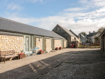 A stone building with blue patio chairs and wooden bench on a concrete courtyard at Poppy Cottage in Llantwit Major