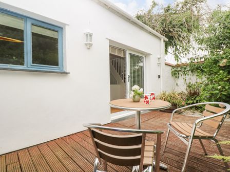 An outdoor patio with a round table, two chairs, a small plant, and two mugs outside sliding glass doors at Bolitho's Retreat in Helford