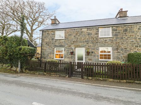 A stone house with four windows a central door and a wooden fence in front at Llwyn Celyn in Brithdir