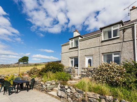 A stone cottage with outdoor patio furniture and garden at Tyn Y Gorlan in Criccieth