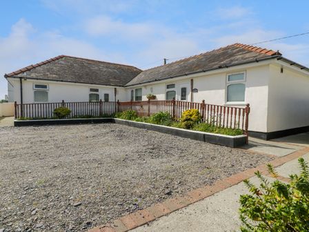 A single story building with a gravel driveway and a wooden railing with plants at Sea Breeze in Dinas Dinlle
