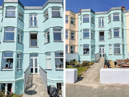 The exterior of a three-story light blue building with multiple windows and a central ramp entrance at Apartment 3 Marian Y Mor in Pwllheli