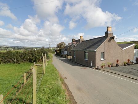 A rural road with houses on one side and a fenced grassy field on the other at Trigfa Cottage in Abersoch