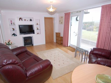 A living room with leather sofas a wall-mounted television and glass door with curtains at Garden View in Kingskerswell