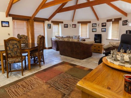A living room with exposed wooden beams sofa set dining table with chairs and window blinds at Hideaway in Tintagel