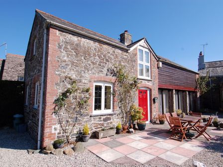 A stone and brick house with a red door and an outdoor patio with a wooden table and chairs at Jacobs Barn in Lifton