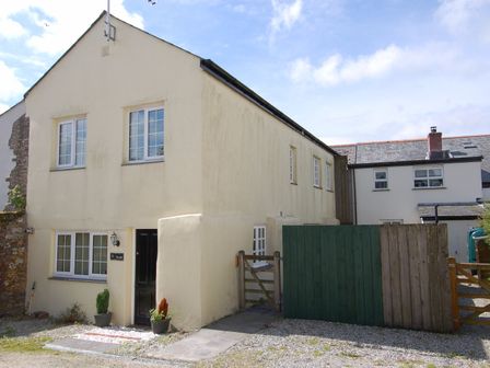 An exterior view of a light yellow two story house with multiple windows a black door and a wooden fence at The Barn in Tregoodwell