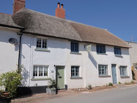 A thatched roof cottage with white walls and multiple blue and green doors and windows at Robyn Cottage in Otterton