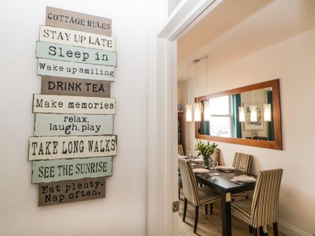 A dining room with a black table set for six and a large mirror on the wall with a sign displaying cottage rules on the adjacent wall at Quayside Lookout in Brixham