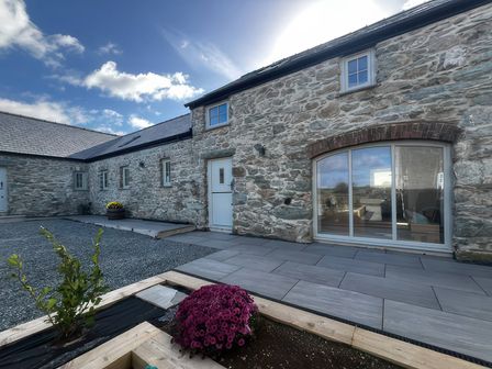 An outdoor area with a stone wall and flower bed at Storws Tanrallt Llanfachraeth