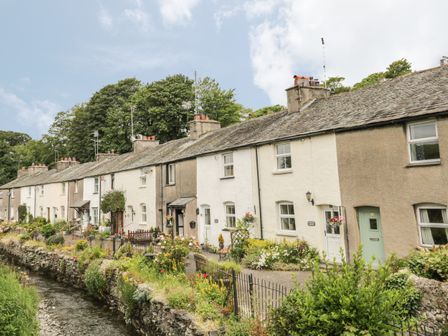 A row of cottages with gardens along a small stream at Herdwick Cottage in Cark in Cartmel