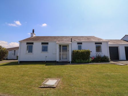 A white single-story house with a central entrance door windows and a lawn in front at Bwthyn Gwyn Bach in Morfa Nefyn