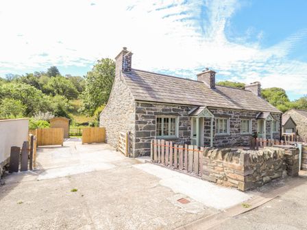 A stone cottage with a slate roof and wooden gates surrounded by trees at Ffrwdd Galed Uchaf in Tregarth