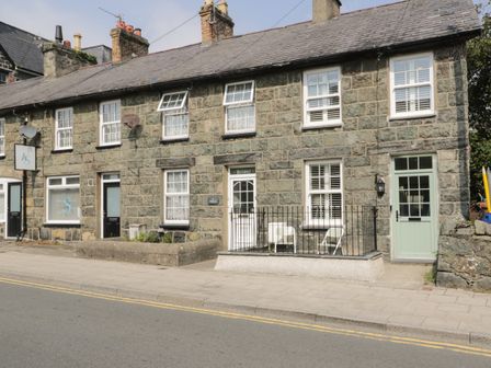 Stone terraced houses with slate roofs and multiple windows along a paved sidewalk at Llawenfan in Criccieth
