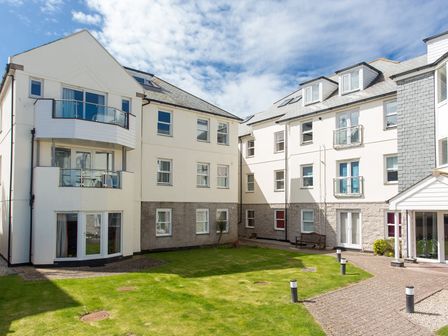 A courtyard with grass and a pathway between white residential buildings at Cribbar View in Newquay