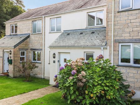 Exterior view of a terraced house with stone walls a white door and a flowering bush in front at Oyster Cottage in Falmouth