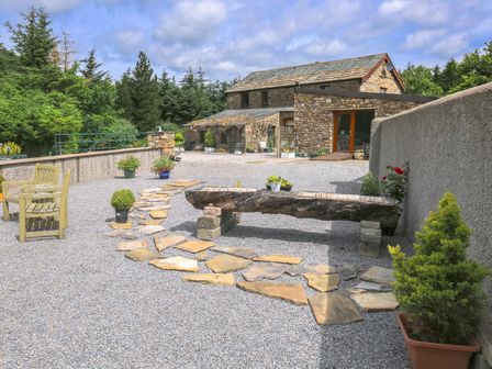 A gravel courtyard with stone path wooden bench chairs and potted plants outside a stone building at Knott Lodge in Sedbergh
