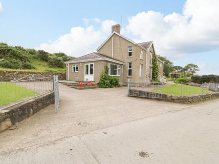 A detached house with a concrete driveway and metal gates surrounded by grass and stone walls at Dinas Farmhouse Annex in Caernarfon