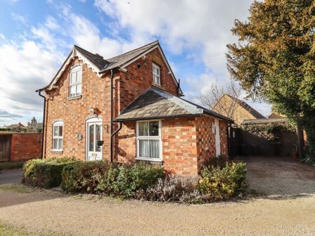 A red brick detached house with a gravel driveway and surrounding bushes at Elder Cottage in Mickleton near Chipping Campden