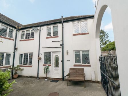 An exterior view of a white two-story building with leaded windows a white door a wooden bench potted plants and a black iron gate at Narnia Cottage in Scarborough