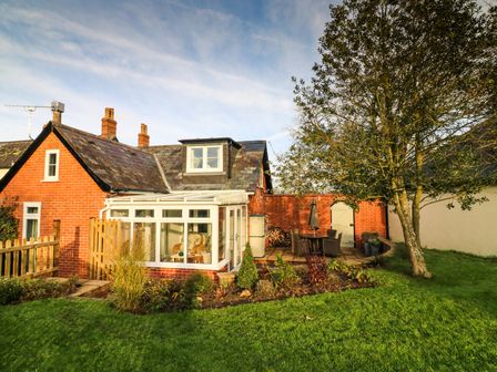 A brick house with a sunroom and patio furniture in a garden at South Lodge in Hazelbury Bryan