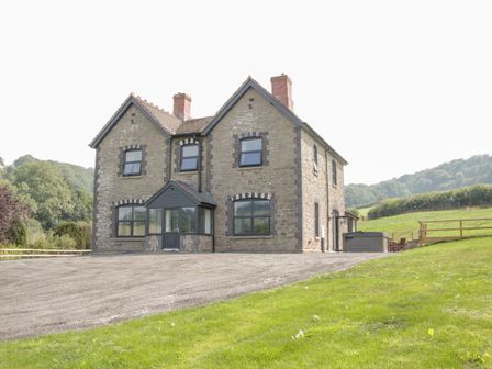 A stone house with multiple windows and two chimneys surrounded by grass and hills at The Farm in Presteigne