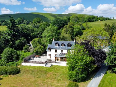 A house with a large patio and surrounding trees near rolling green hills at Oakwood House in Rhayader