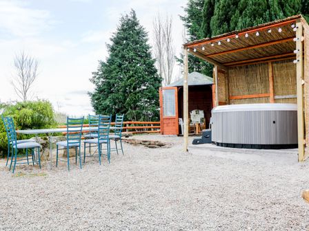 An outdoor area with blue chairs around a table a hot tub under a wooden shelter and a small wooden cabin at Broadway Lands Farm in Little Dewchurch