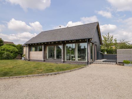 A single story house with large glass windows a gravel driveway and a grass lawn at The Barn at Daubeneys in Colerne