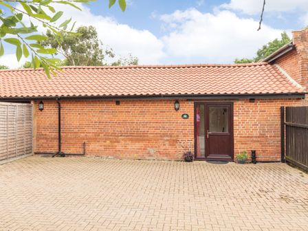 A brick building with a tiled roof and a dark brown door with potted plants on a paved area at The Hen House in Diss near Gissing