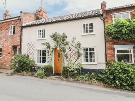 A street view of a white house with a wooden door and plants growing on the wall at Ploughmans in Hoxne