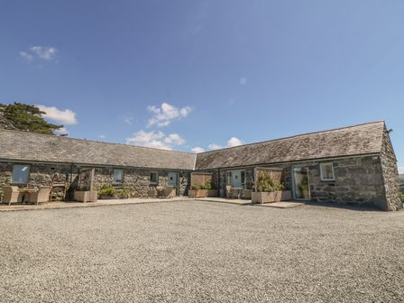 An outdoor view of a stone building with slate roof and patio seating at Cornel Glyd in Talybont near Barmouth