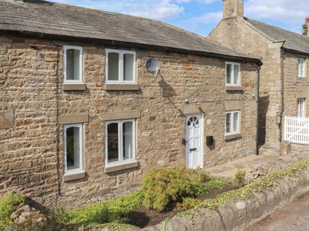 A stone cottage exterior with white windows and door surrounded by a small garden at 1 Dunkirk Cottages in Humshaugh near Hexham