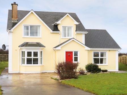 A yellow two-story house with a red front door a driveway and bushes in the front at Benbulben View in Tullaghan County Leitrim