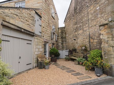 A courtyard with stone walls two wooden benches potted plants and shutters on windows at The Olde Stables in Warkworth