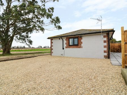 A gravel area next to a single story building with a window and an antenna near a tree and open field at The Stable at Church Farm House Limpenhoe near Reedham