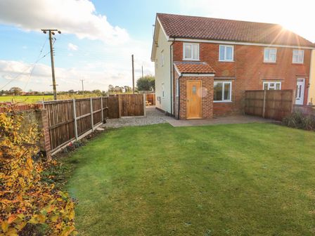 A backyard with a lawn and wooden fences next to a semi detached house at 27 Whitegates in Ludham