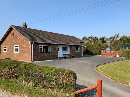 A single-story brick house with a tiled roof a front driveway a bench two potted plants a hedge and a red wooden gate at Blaenywawr in Lampeter