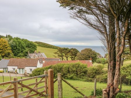 A countryside scene with houses trees a wooden gate and a view of the sea at Wren Cottage in Ilfracombe