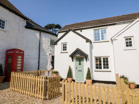 A white house with a green door and wooden fence with a closed patio umbrella and red telephone booth outside at Swallow Cottage in Ilfracombe